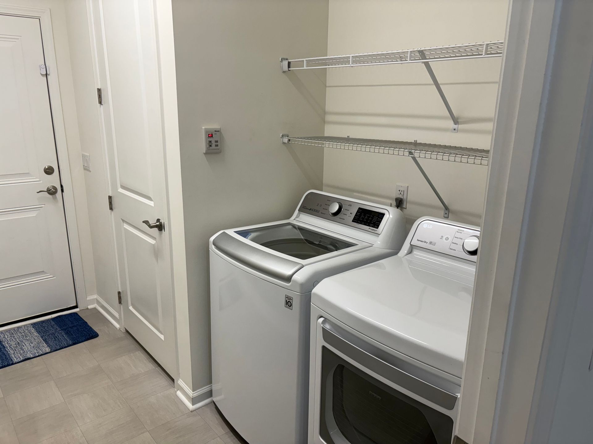 Laundry room with white washer and dryer, shelves, and a door.