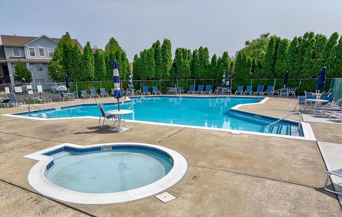 Outdoor pool with lounge chairs, umbrella, and a smaller hot tub.