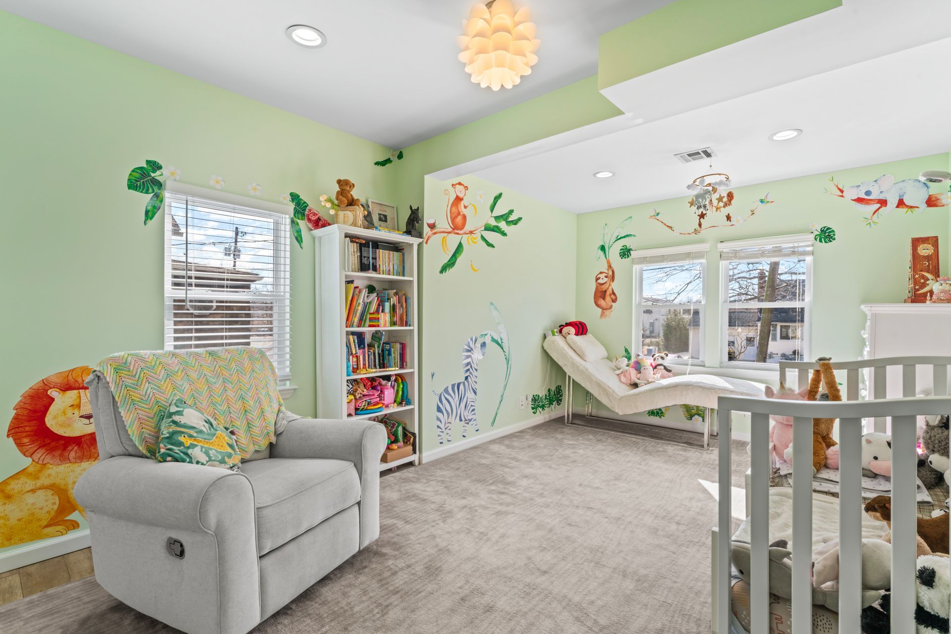 Nursery with green walls, animal wall art, recliner, crib, and a chaise lounge.