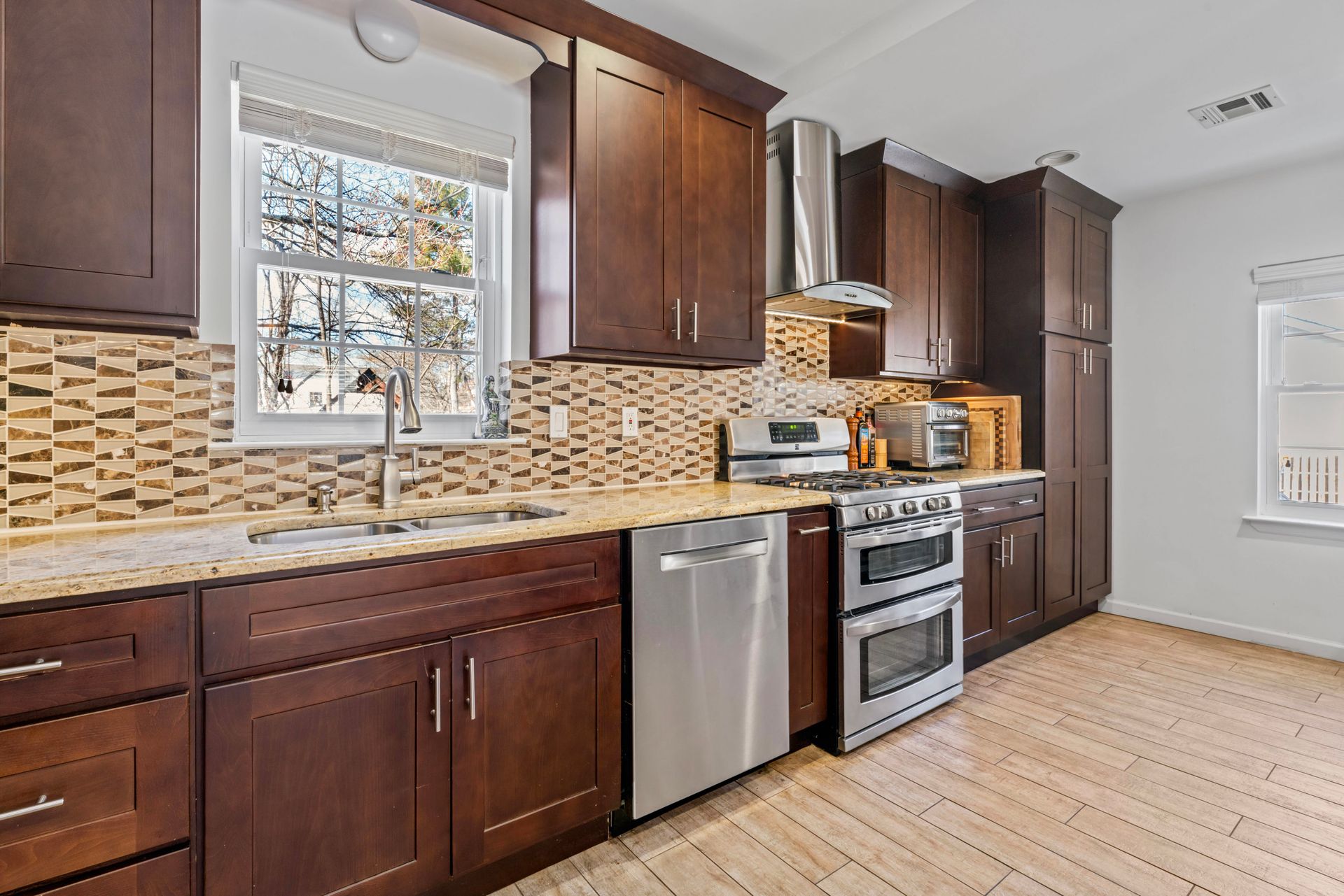 Kitchen with dark wood cabinets, stainless steel appliances, tan backsplash, and a window.