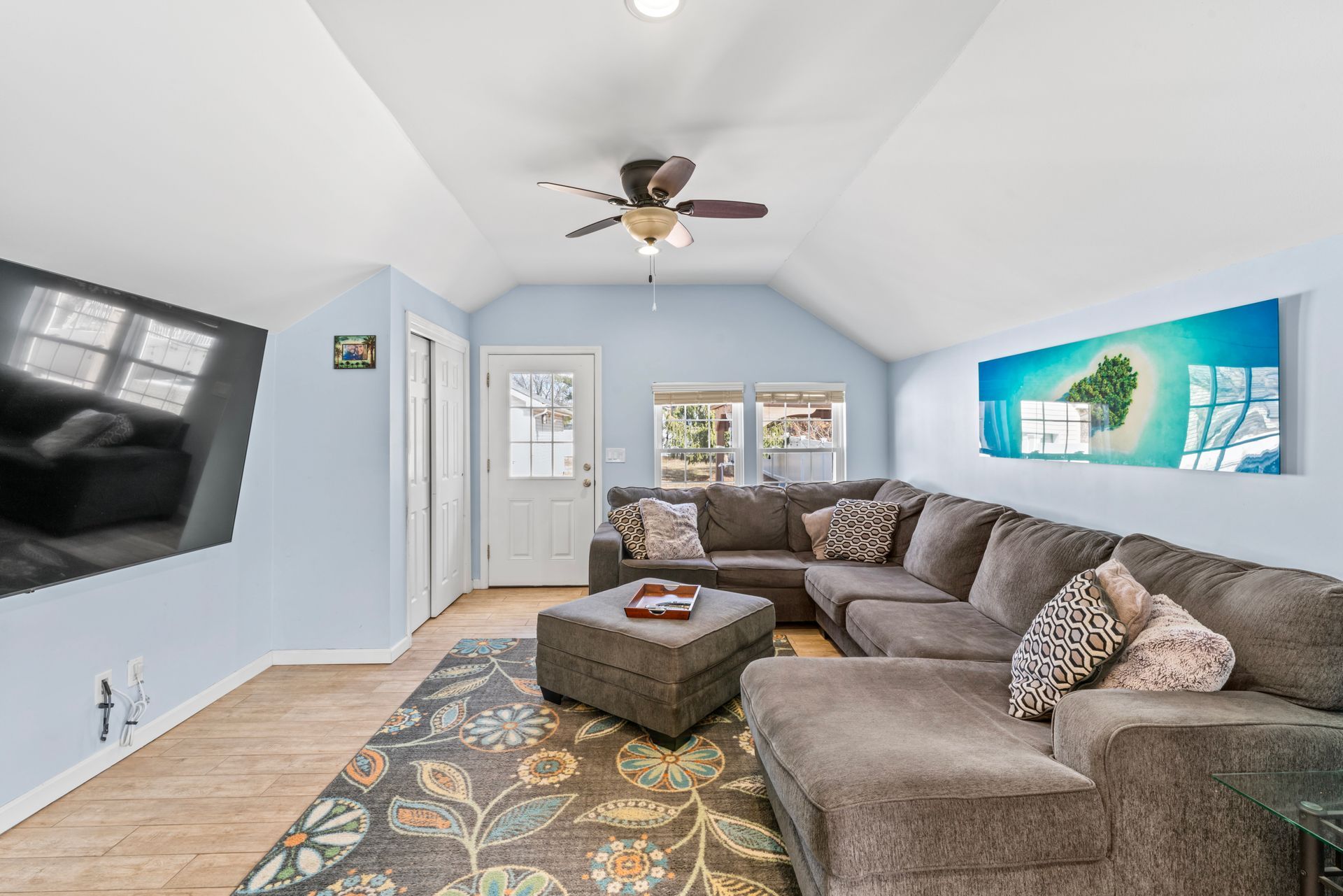 Living room with gray sectional sofa, TV, rug, and artwork. Blue walls and vaulted ceiling.