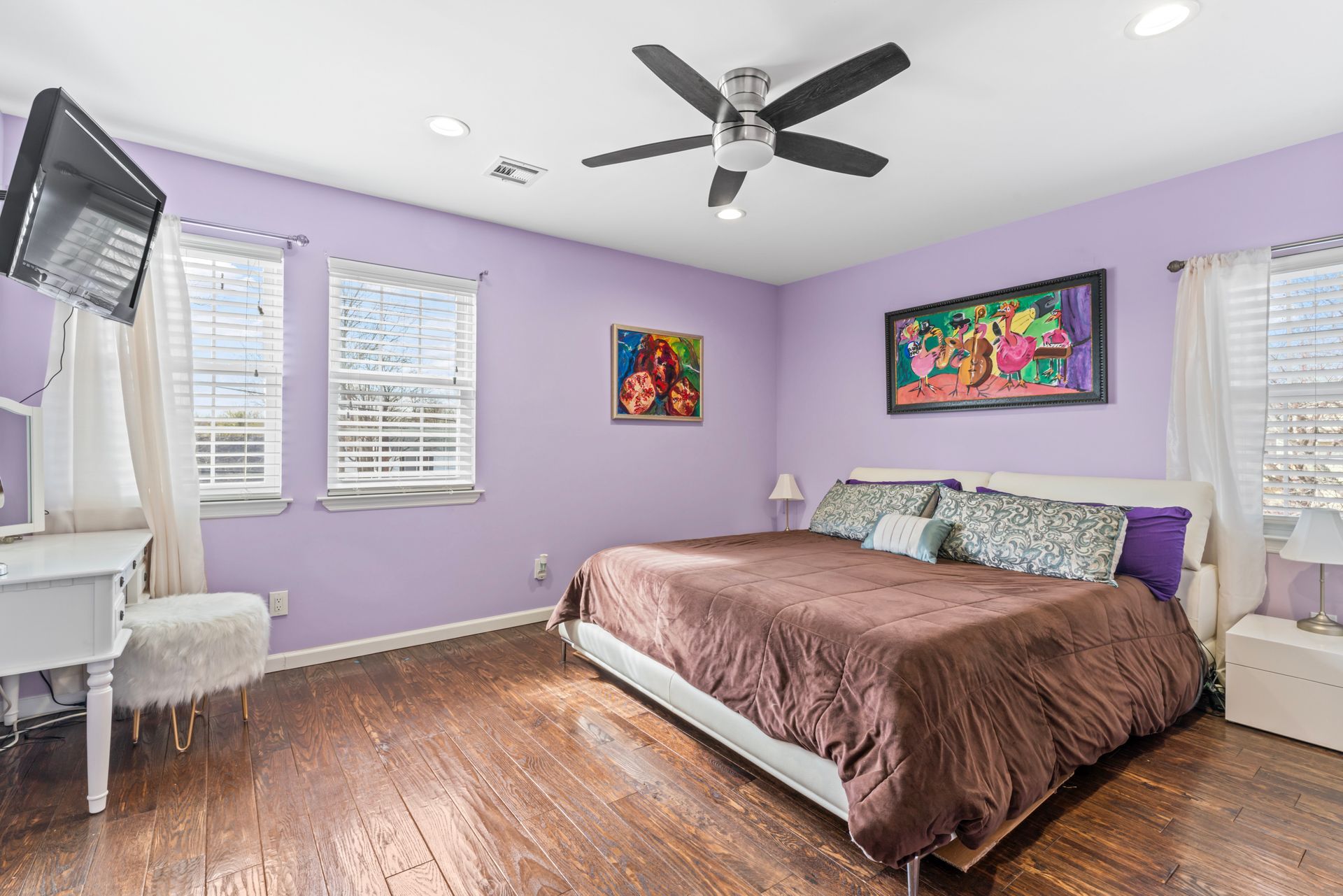 Bedroom with lilac walls, hardwood floor, bed with brown comforter, and a mounted TV.