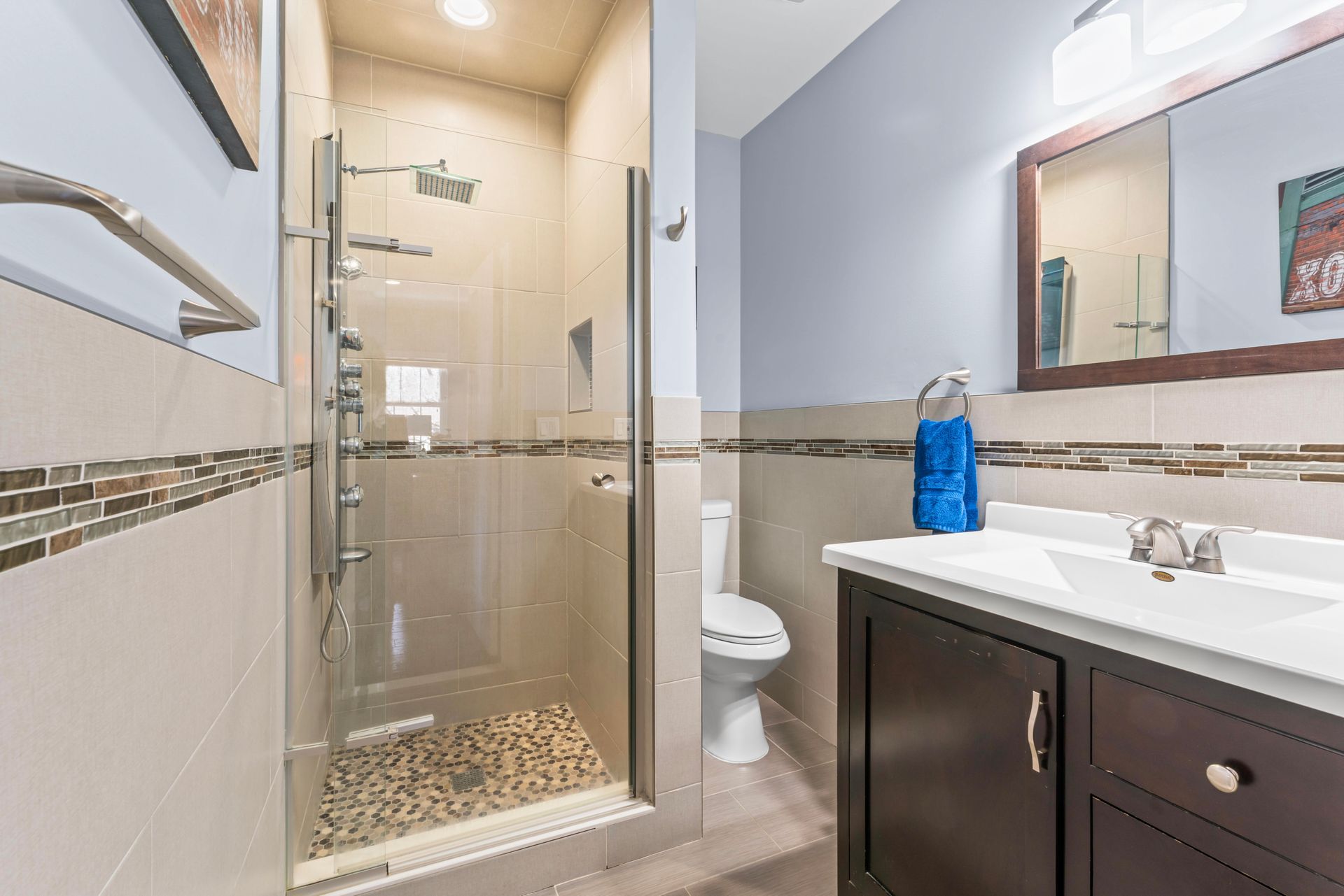 Bathroom with glass shower, dark vanity, and toilet, featuring light-colored walls and tiled accents.