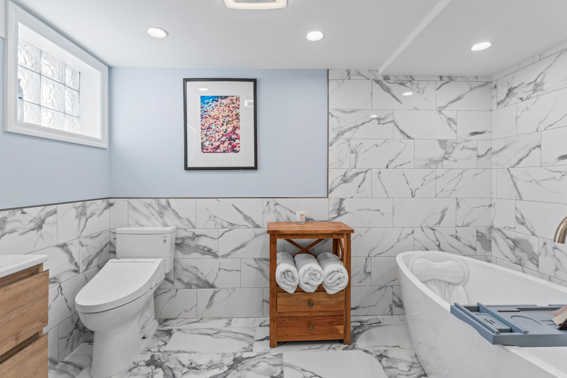 Modern bathroom with marble tile, a white bathtub, and a wooden towel rack.