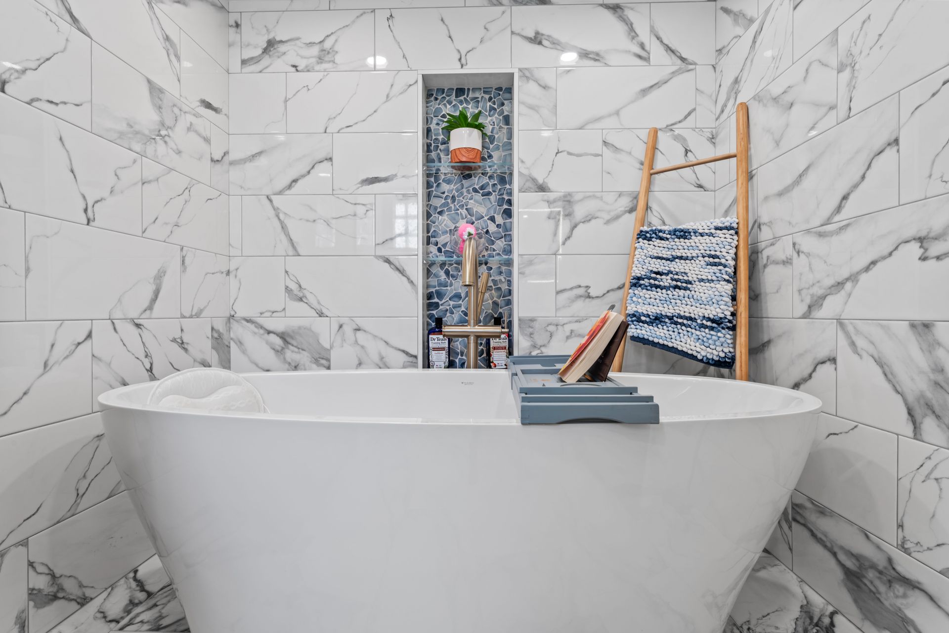 White modern bathroom with marble tile, a freestanding tub, and a decorative ladder.