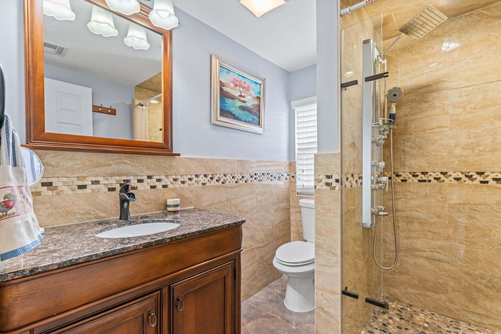 Bathroom with brown vanity, granite countertop, toilet, and shower with stone tile.