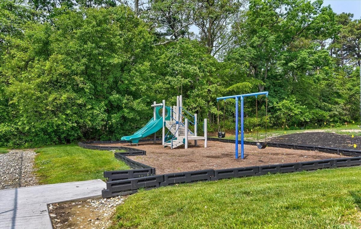 Playground with slide, climbing structure, and monkey bars, set against a backdrop of trees and a green lawn.