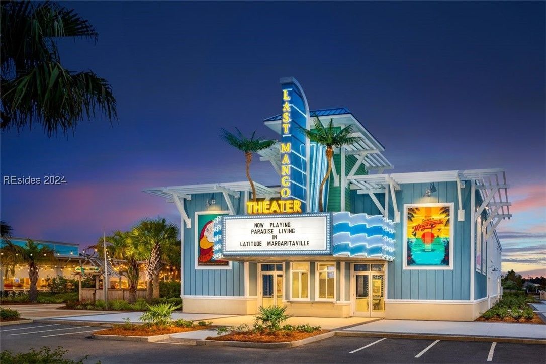 Blue, beach-themed theater with a lit marquee. Palm trees and a sunset sky frame the building.