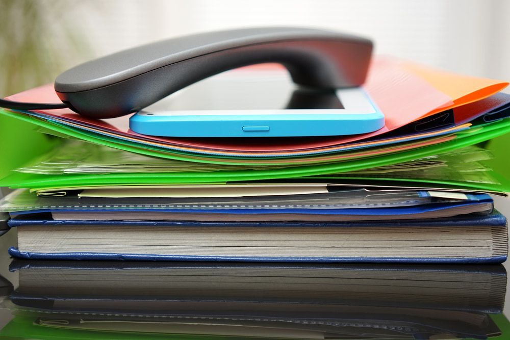 Telephone handset, smartphone, and assorted files stacked on a reflective surface. — Sunshine Office Solutions in Nambour, QLD