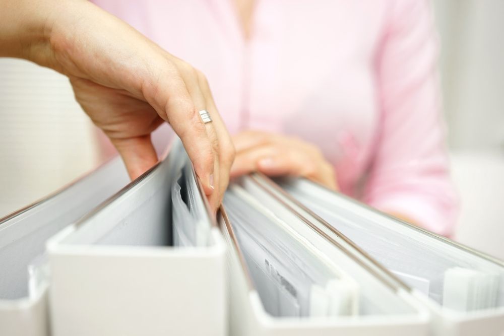 Hand reaching into a white binder, sorting through documents. Pale pink shirt visible. — Sunshine Office Solutions in Maroochydore, QLD