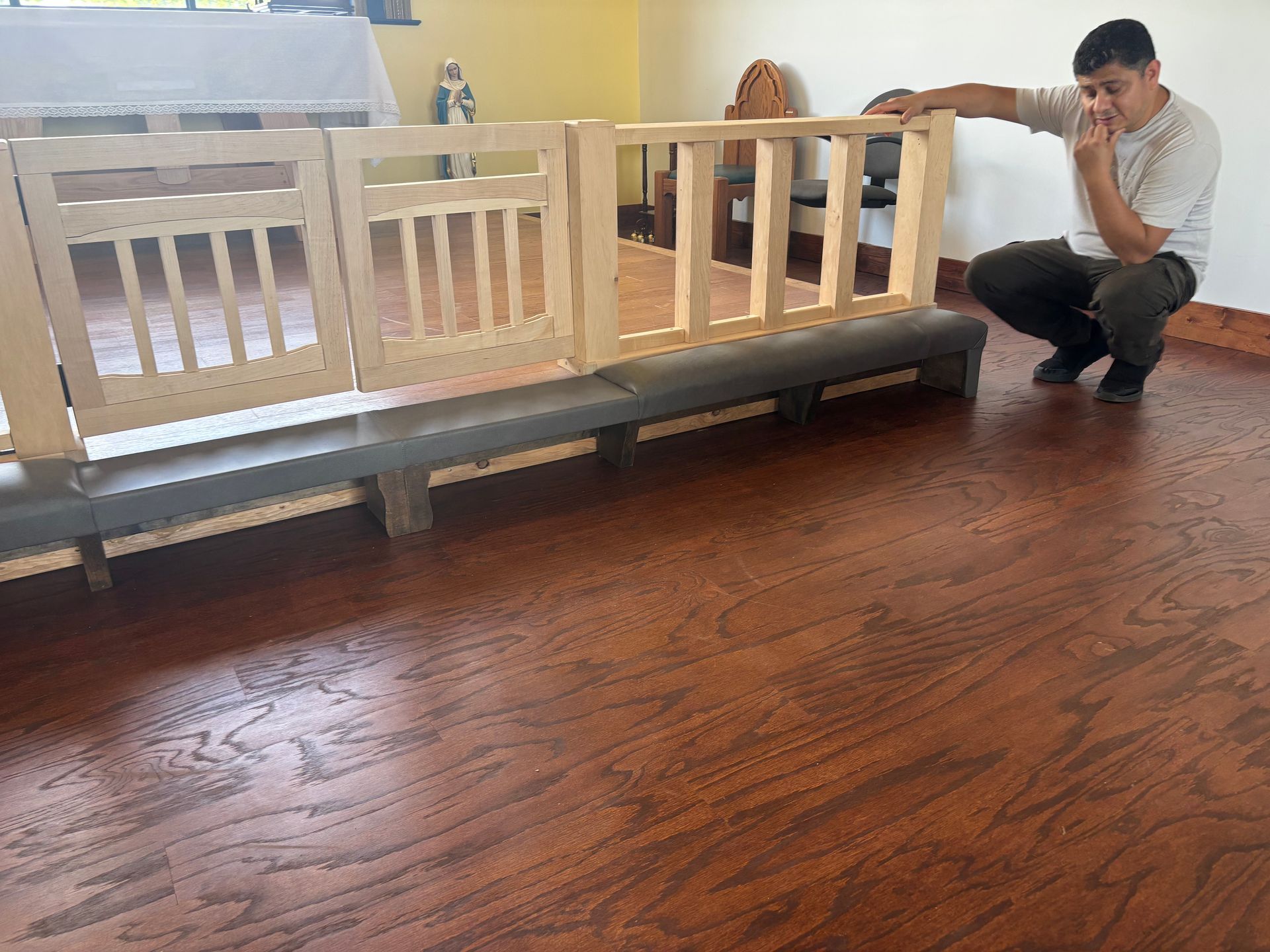 Man crouching beside a white wooden playpen on a polished wooden floor indoors
