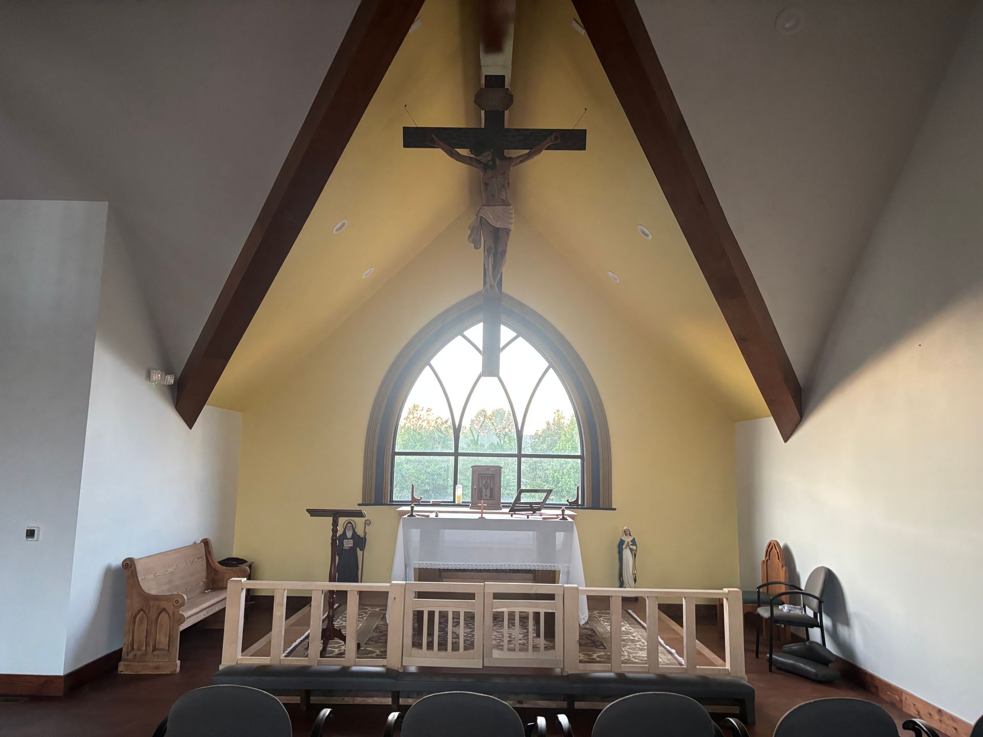 Small chapel interior with altar, crucifix, and arched window beneath a steep wooden ceiling