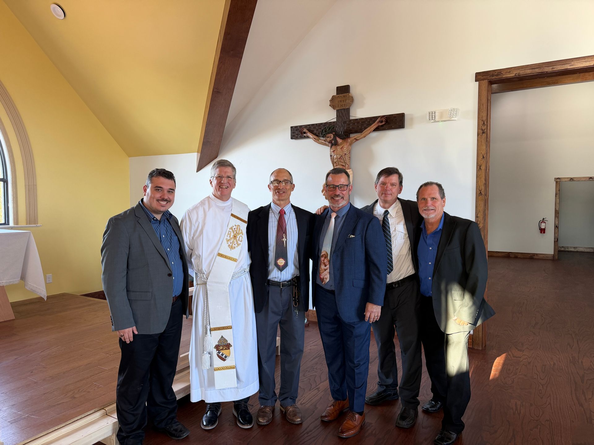 Five men standing in a church interior, with a crucifix on the wall behind them