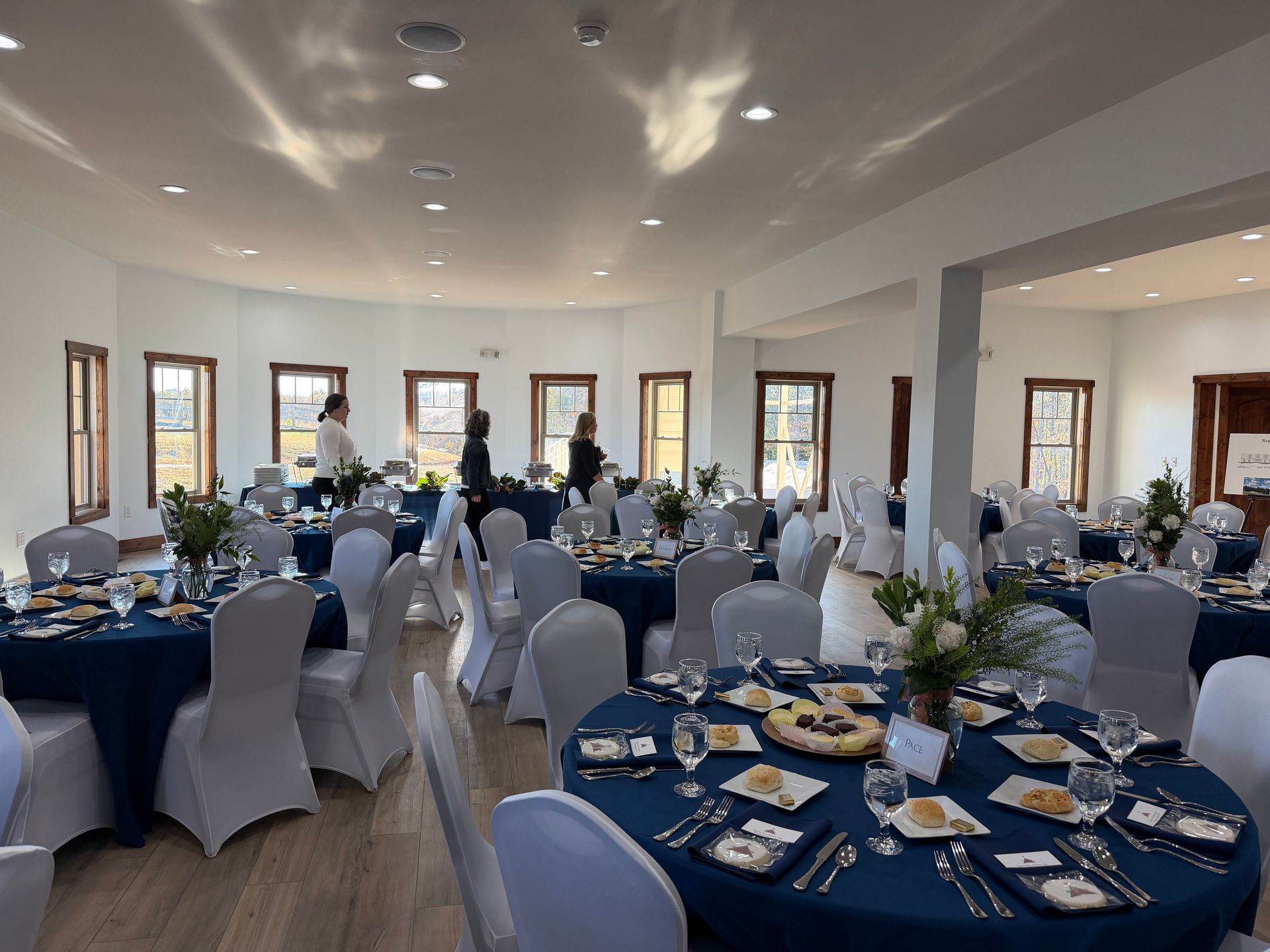 Banquet hall set for an event with round tables, white chair covers, and blue table settings