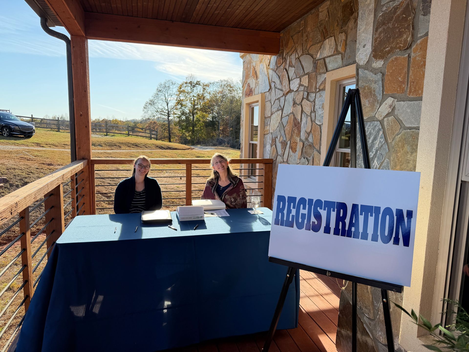 Registration table under a porch with two staff members and a large “REGISTRATION” sign on an easel