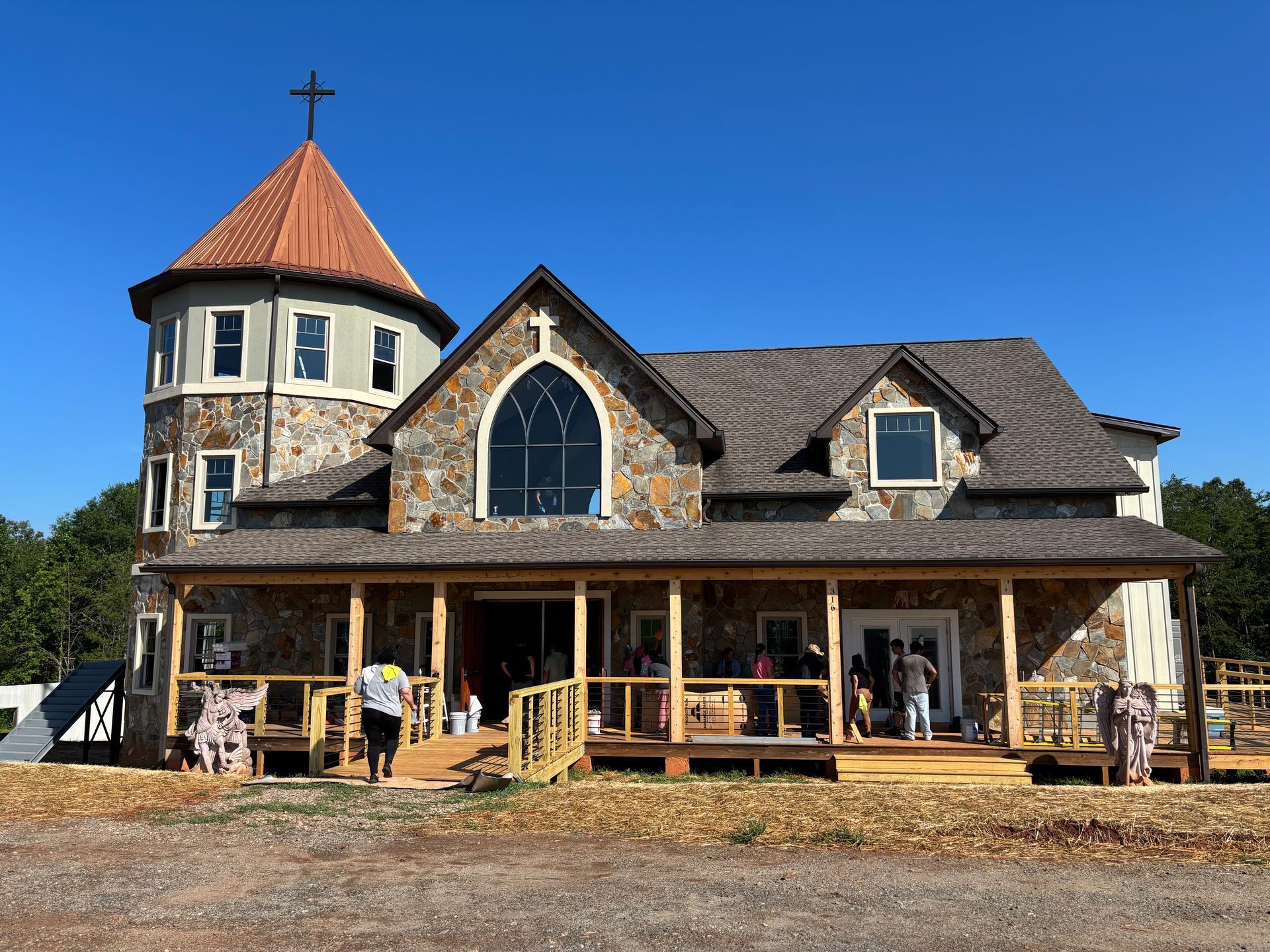 Rustic stone church building with a round tower and orange roof under a clear blue sky