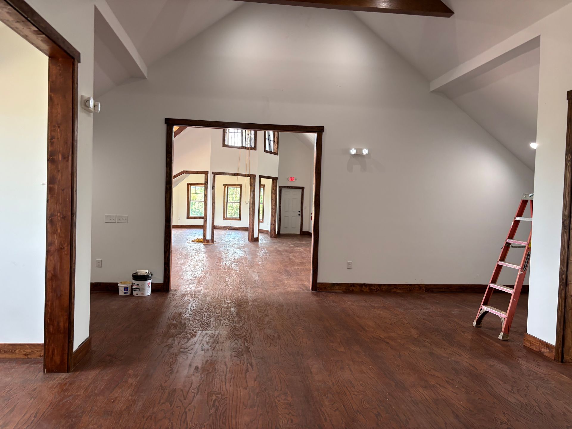 Spacious empty room with wood floors, white walls, exposed beams, and a red ladder near the right wall.
