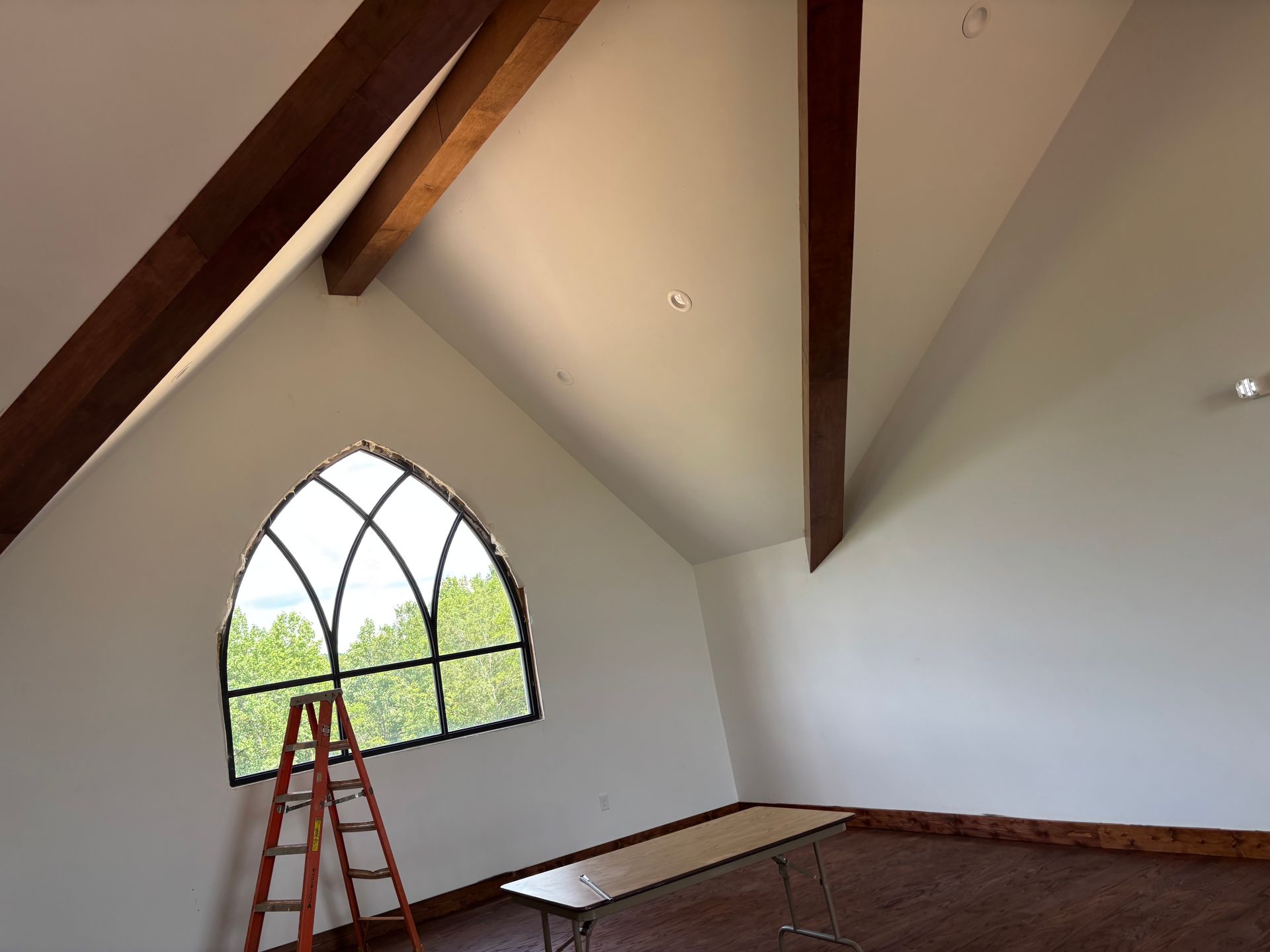 Attic room with exposed beams, arched window, and a red ladder on the floor