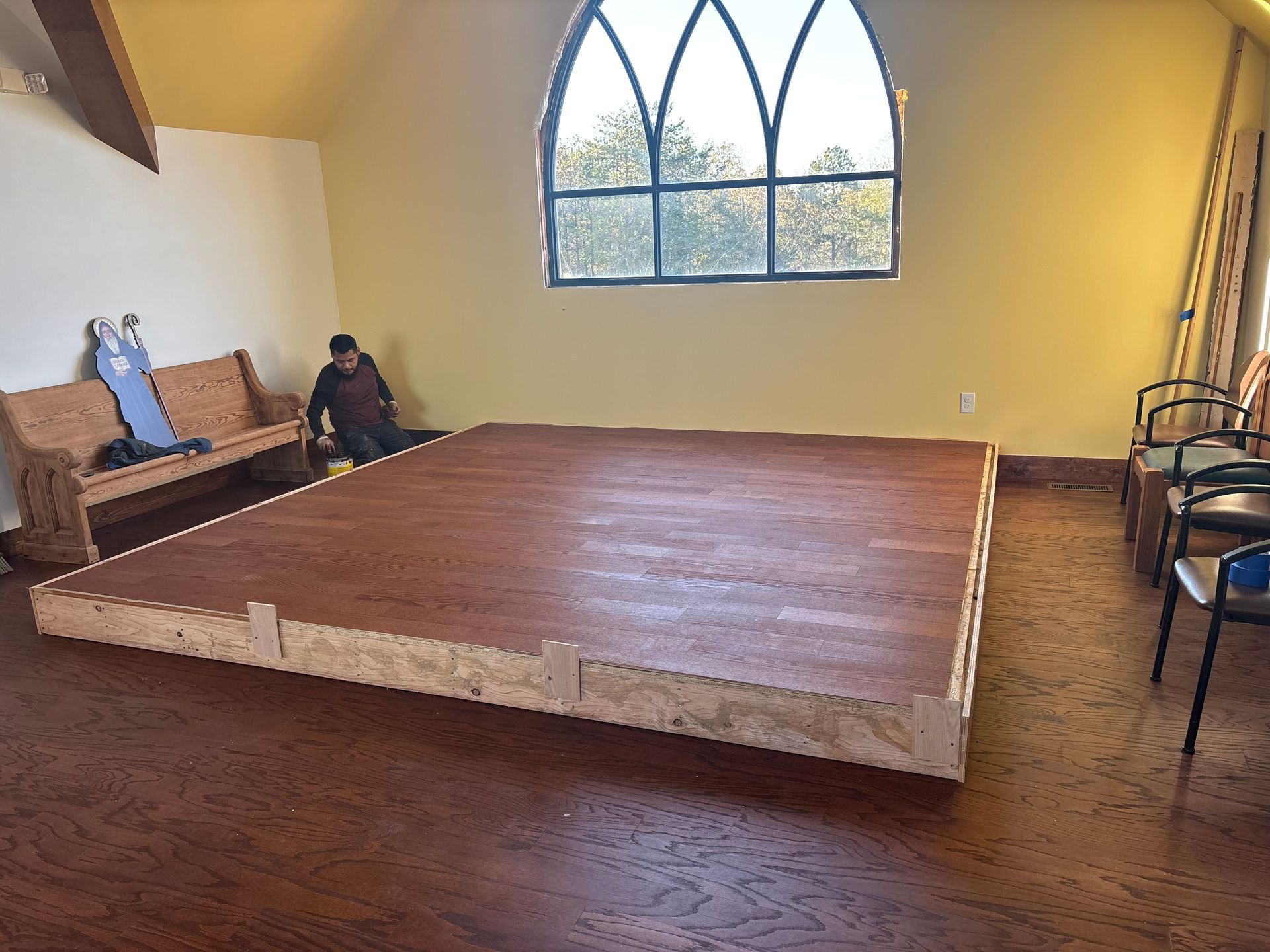 Bedroom with a low wooden bed platform, large arched window, and seating along the wall.