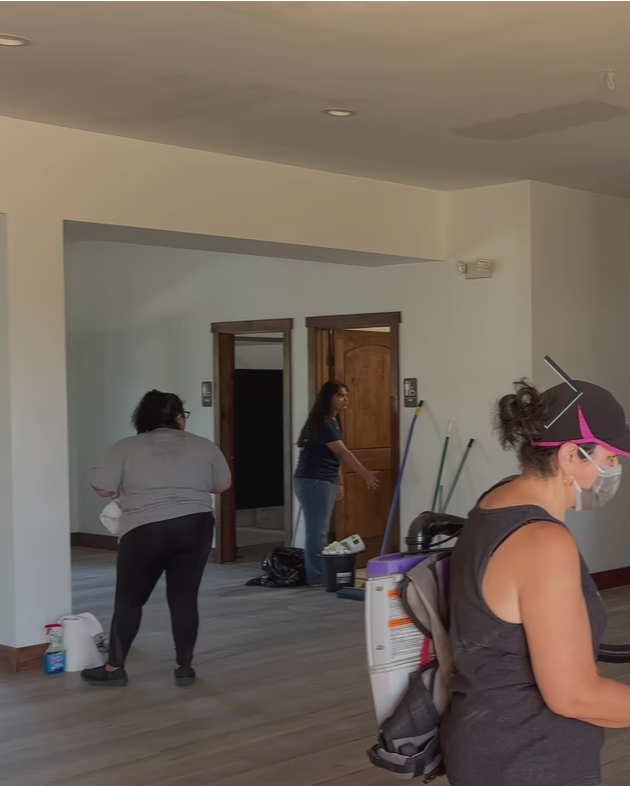 People painting walls and working inside an unfurnished room under renovation.