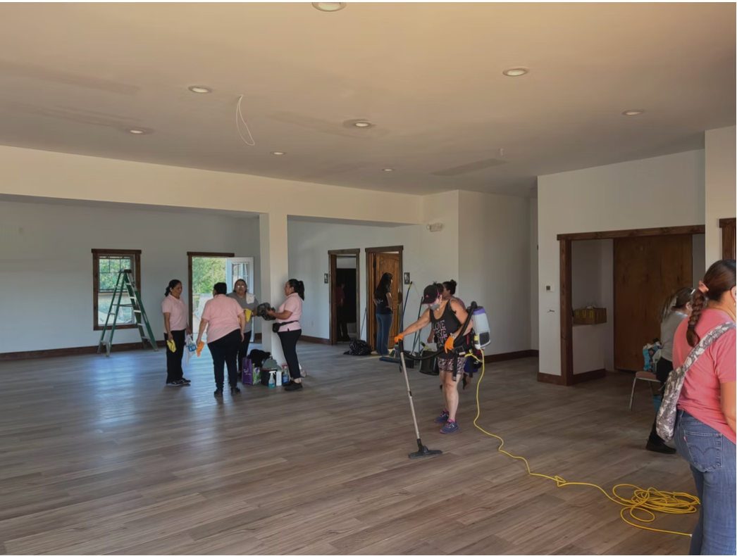 People setting up equipment in a large empty room with wood floors and white walls