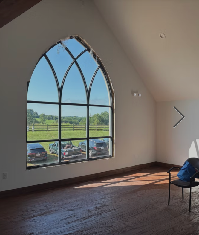 Bright room with arched window overlooking a green field, wooden floor, and a chair by the wall.