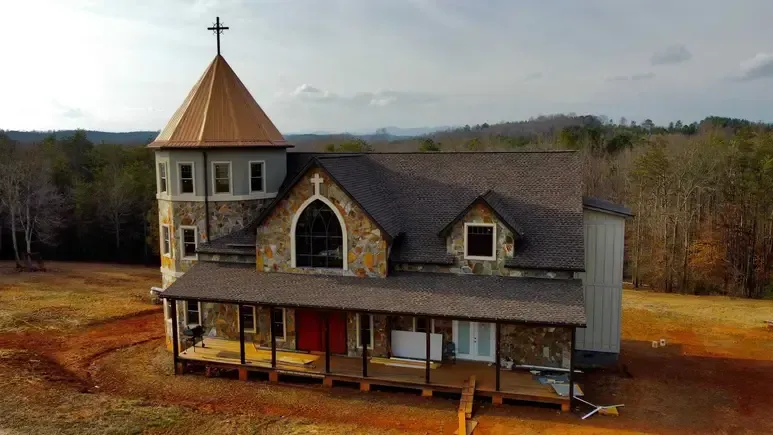 Small church with a copper steeple on a rural hillside, surrounded by bare trees.