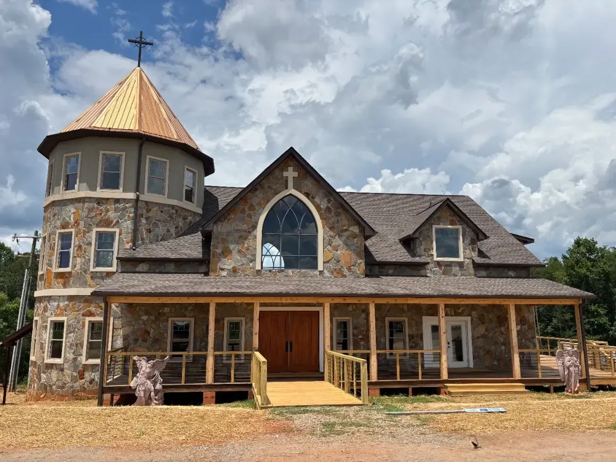 Stone church with a round tower, steep roof, and wooden porch under a cloudy sky