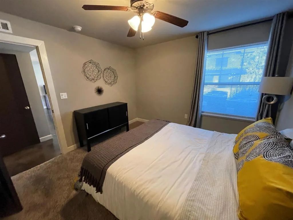 Bedroom with bed, dresser, window with curtains, and ceiling fan.