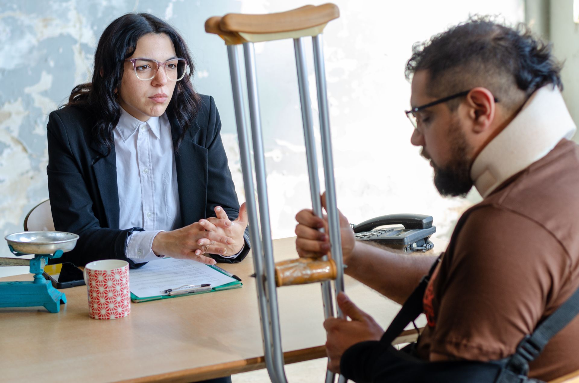 An injured man with a neck brace and crutches sits in front of a female lawyer in a suit.