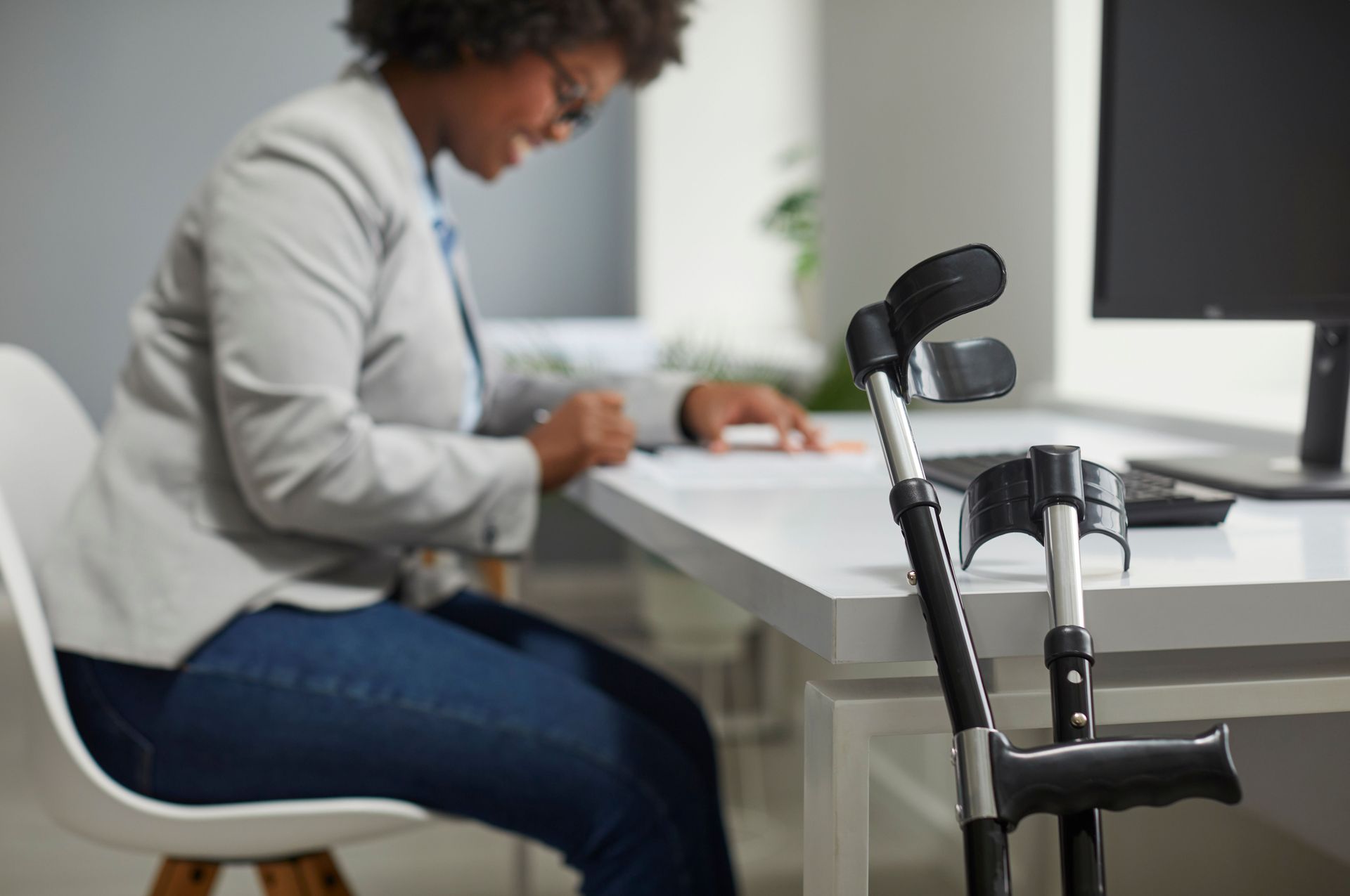 Person working at a desk beside a forearm crutch in a bright office