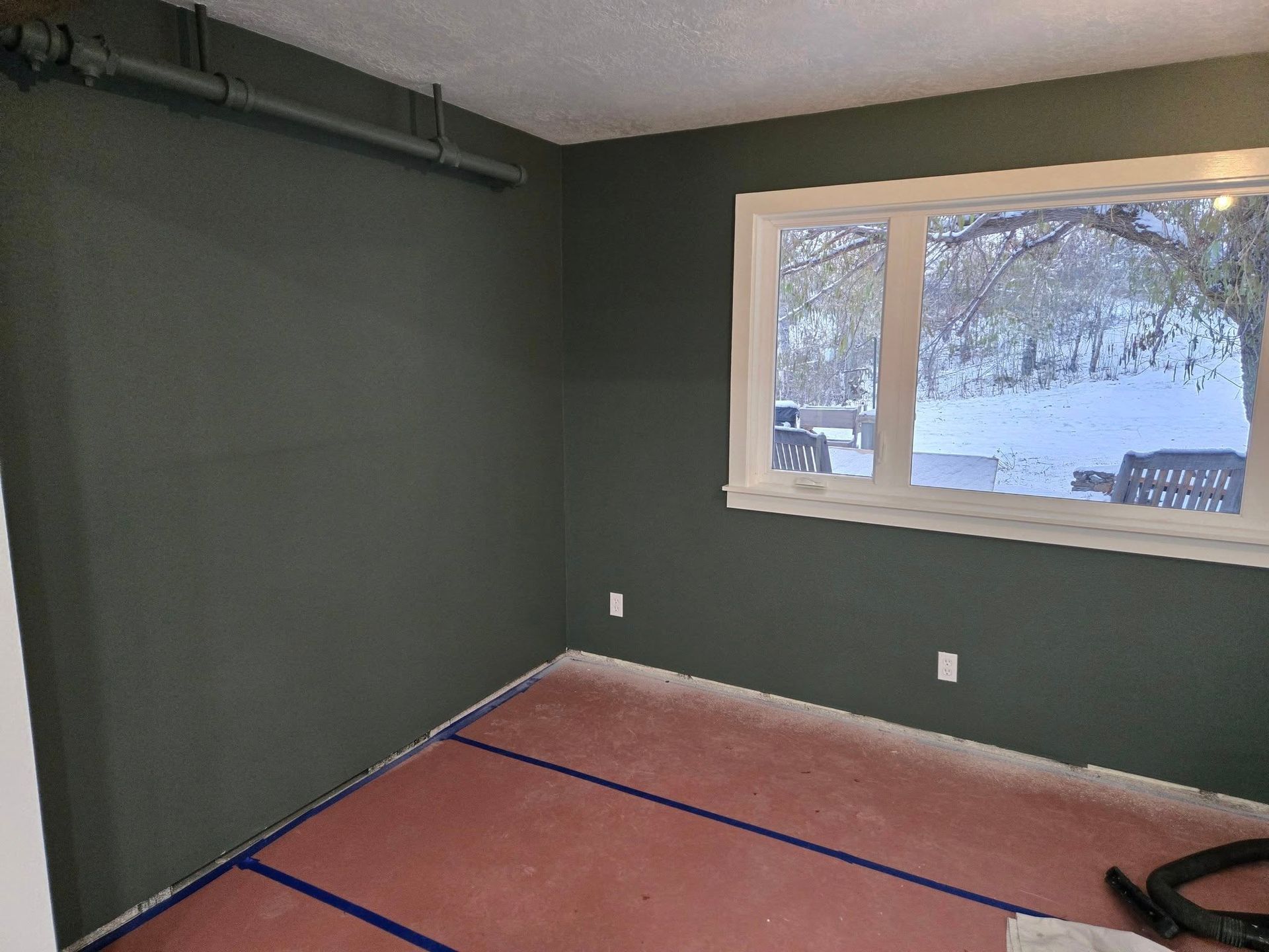 Empty room painted dark green, with white window frame and pink floor covering.