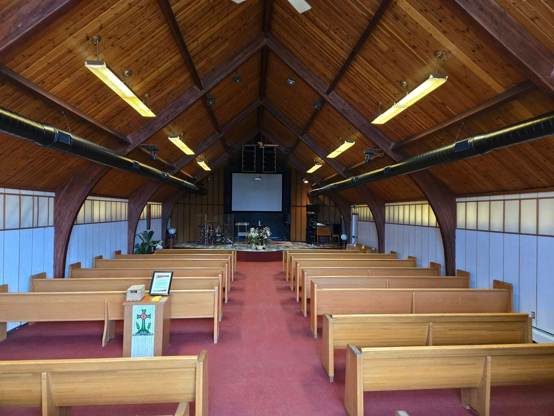 Interior view of a church with wooden pews, red carpet, stage, and a wooden vaulted ceiling.