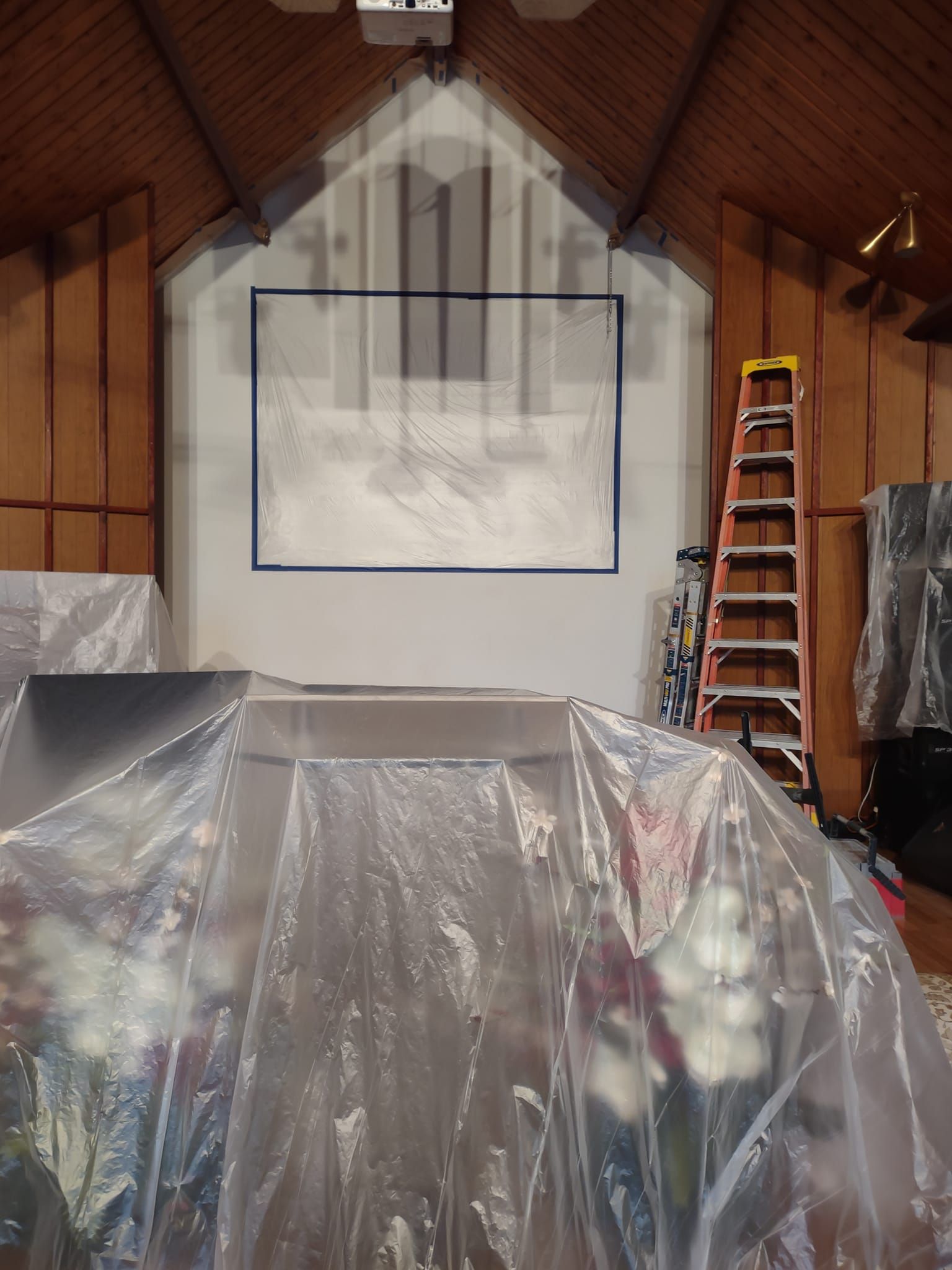 Interior of a church during renovations. Covered altar and a ladder are present; the wall has blue tape.