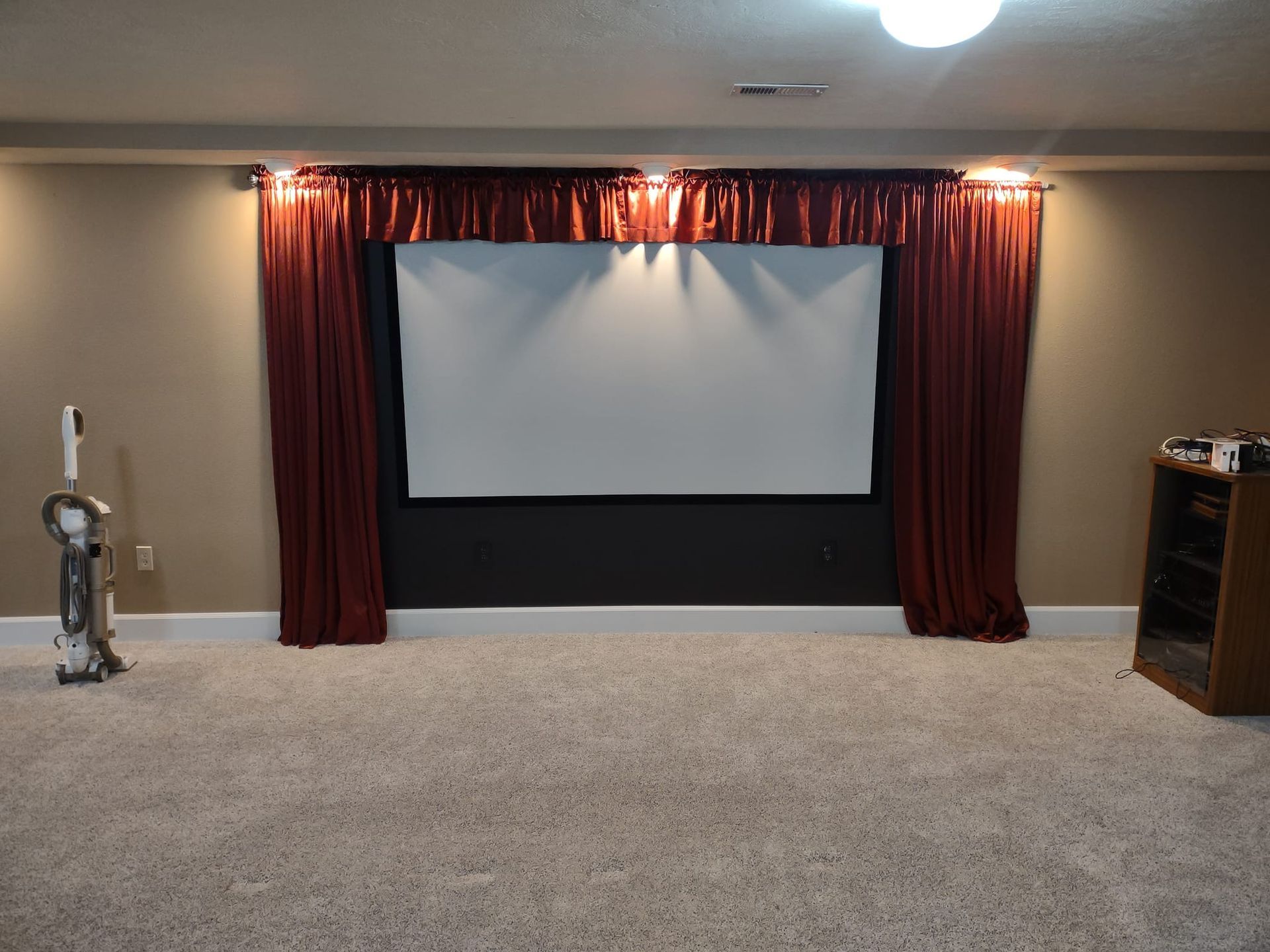 Home theater setup with a screen, red curtains, and beige carpet.