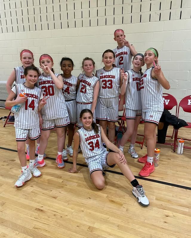 Youth basketball team posing with coach in black-and-red uniforms on a gym court