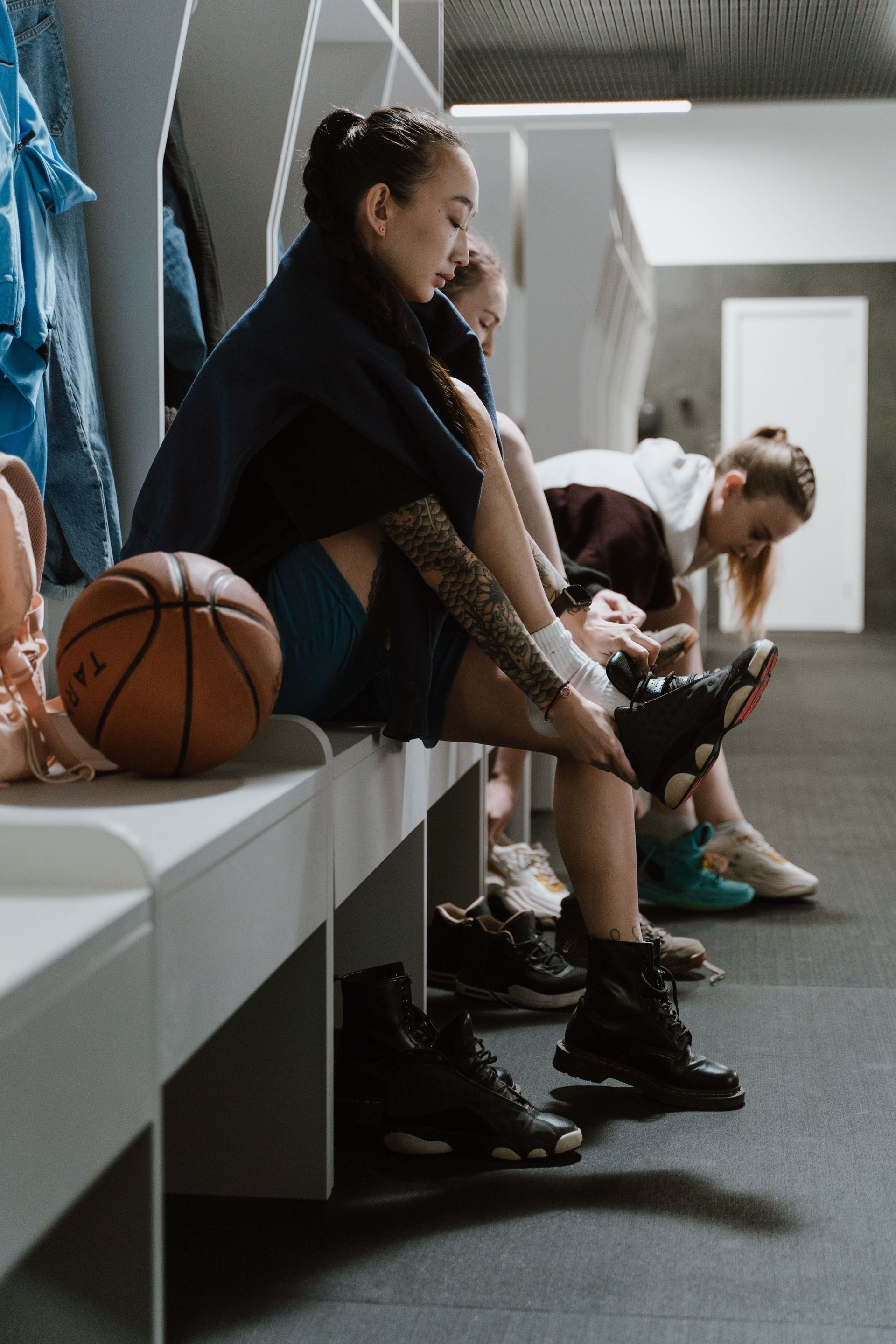 Athletes sitting on a locker room bench, lacing up cleats beside a basketball.