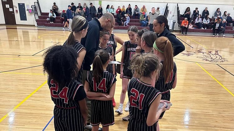 Youth basketball team huddles with coach on a gym court during a game timeout