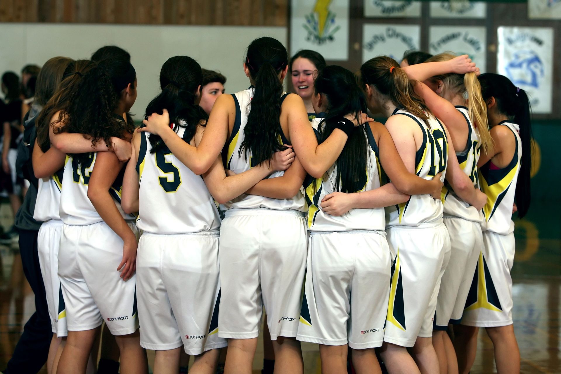 Basketball team huddled in white uniforms, celebrating together on the court.