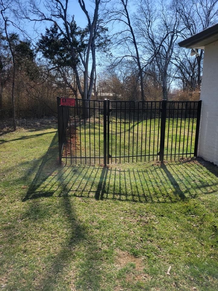 A black fence is surrounding a lush green yard with trees in the background. Middle, TN