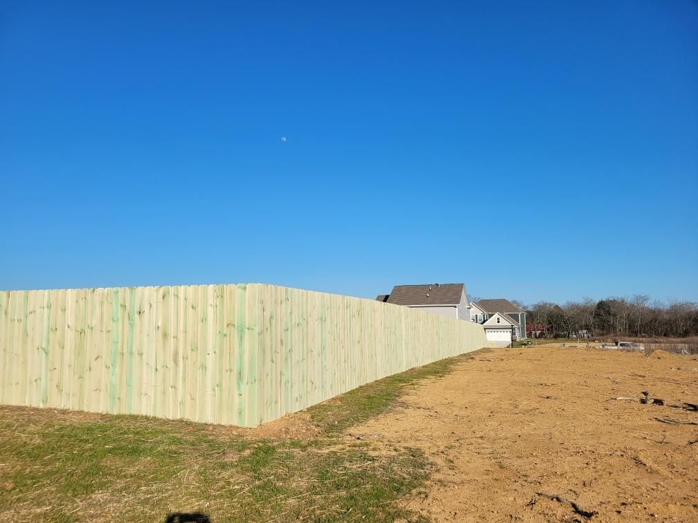 A wooden fence surrounds a dirt field with a house in the background. Middle, TN