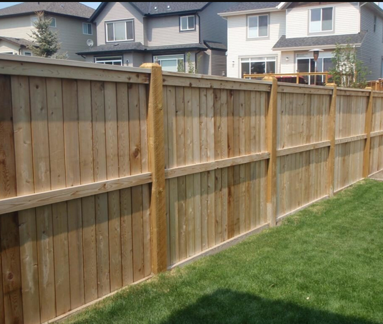 Wooden privacy fence along a green lawn with houses in the background
