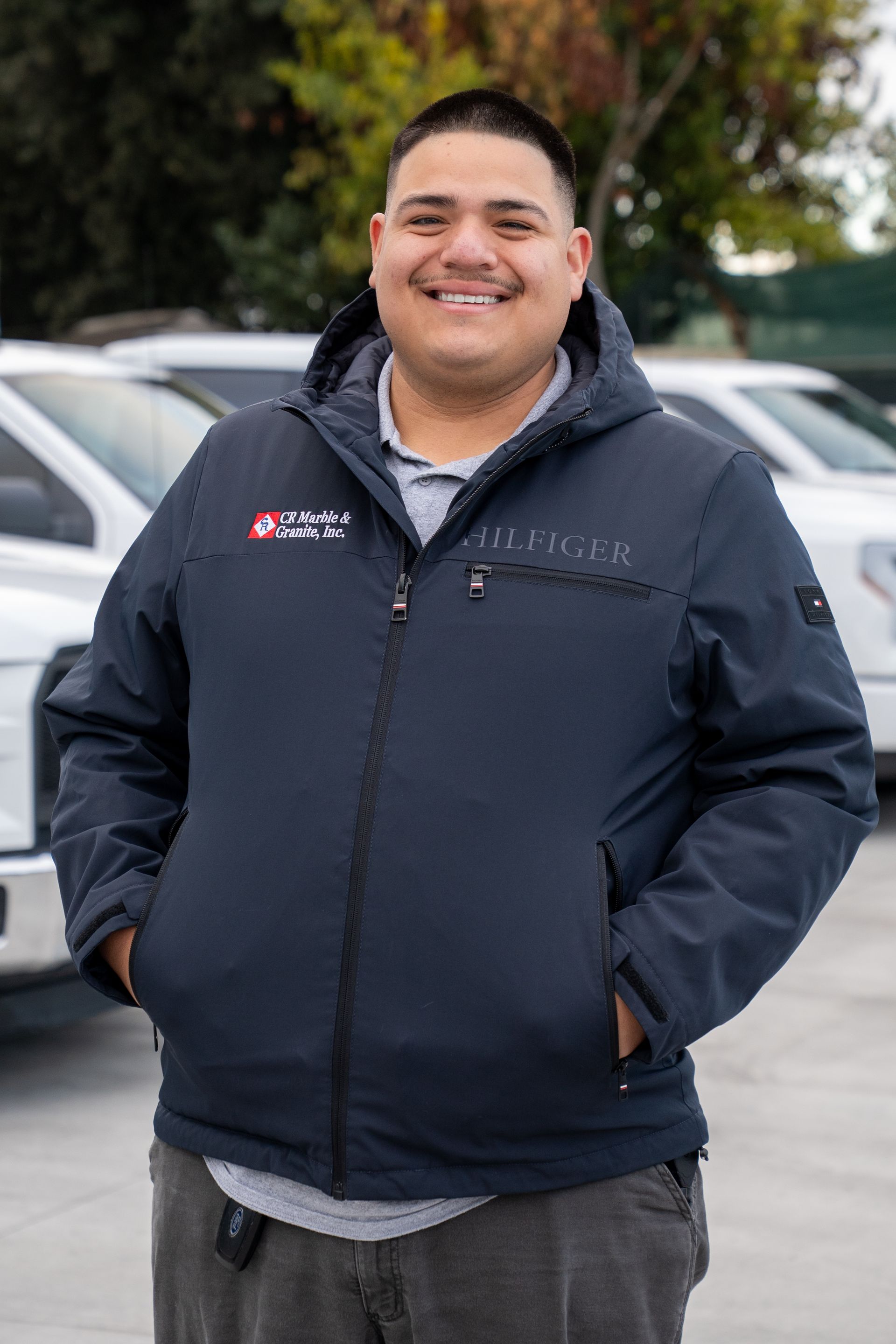 A man in a blue jacket is standing in front of a row of white trucks.