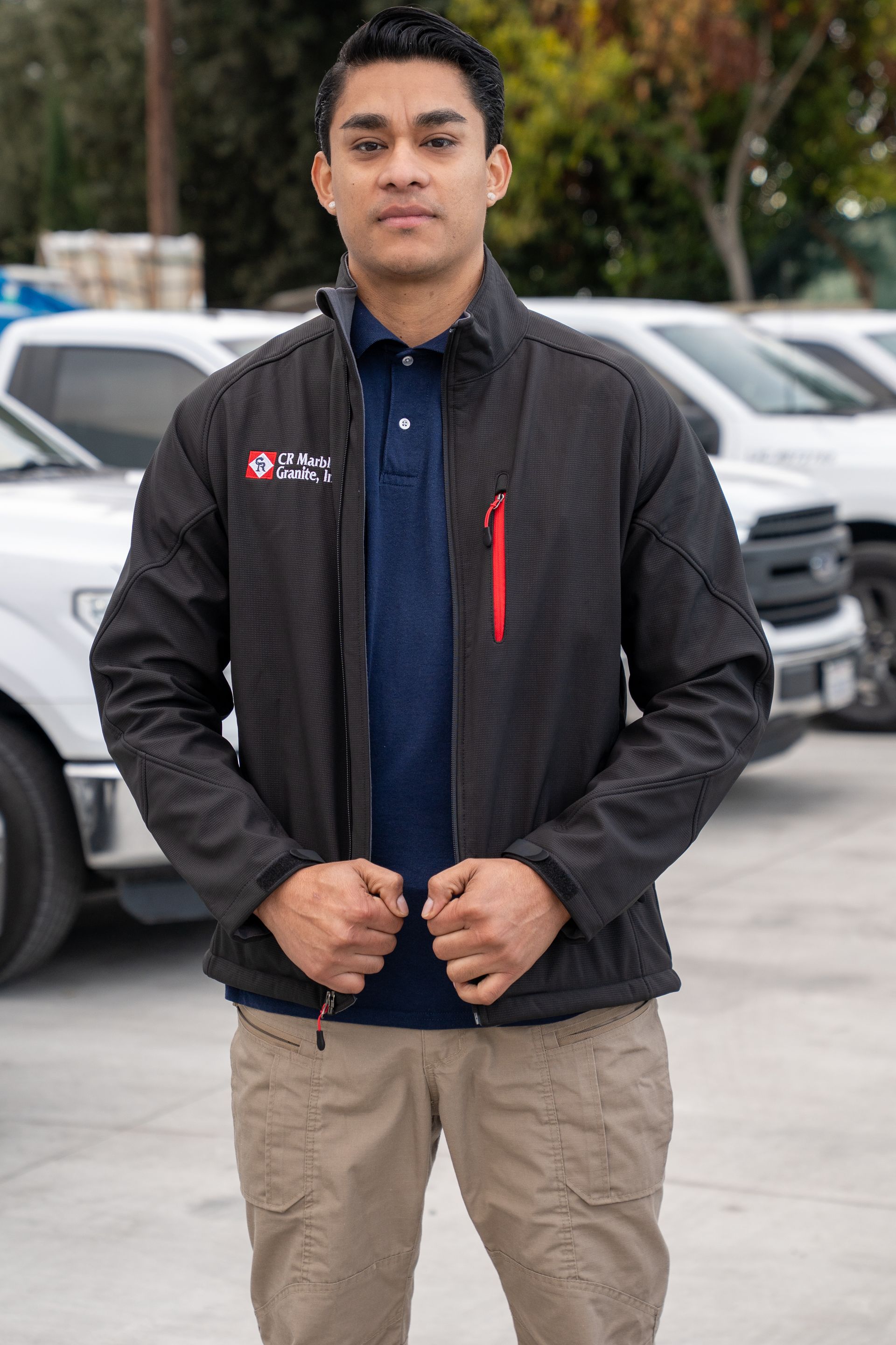 A man in a black jacket is standing in front of a row of trucks.