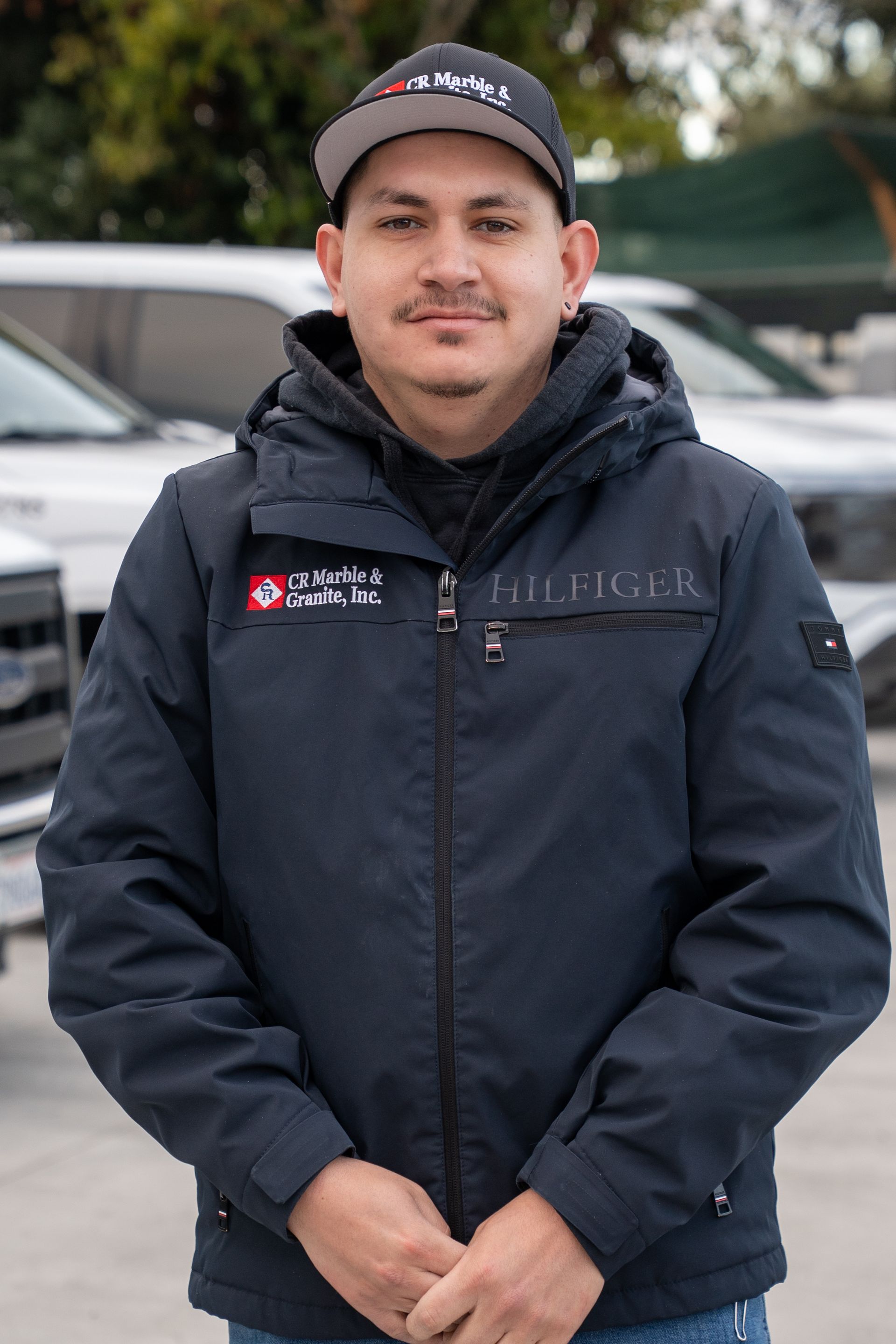A man wearing a hat and a jacket is standing in front of a row of cars.