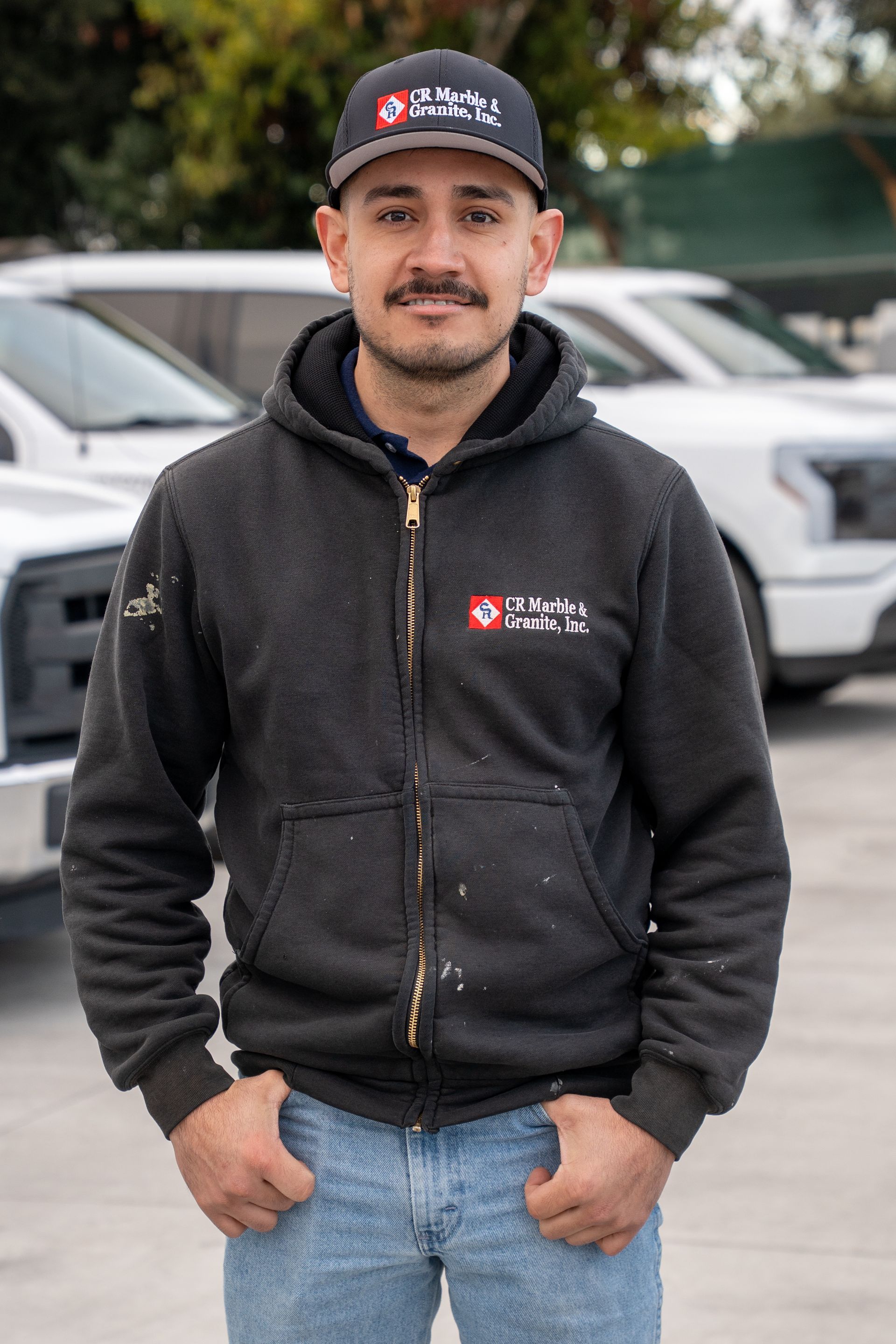A man wearing a hat and a hoodie is standing in front of a row of cars.