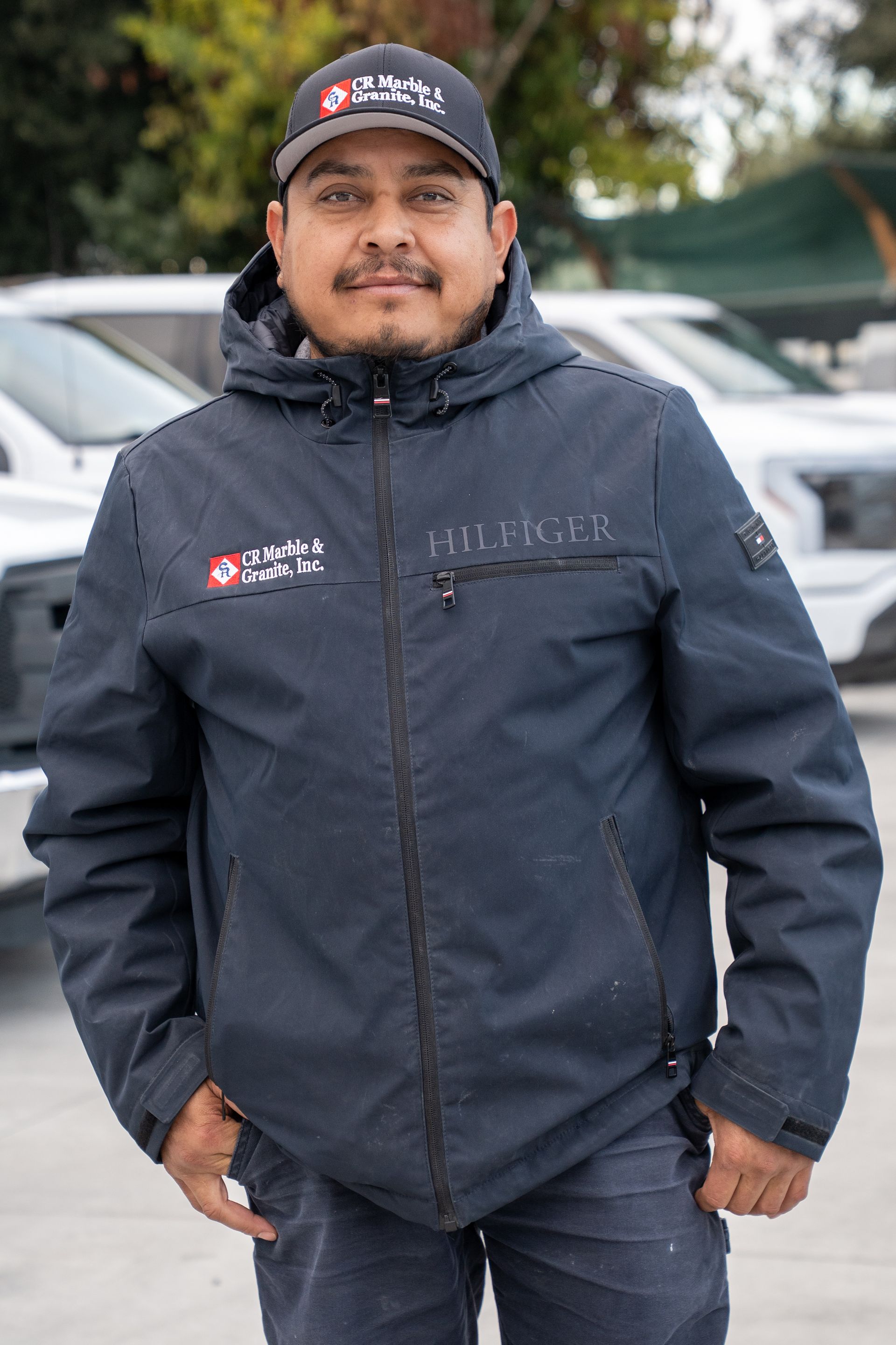 A man wearing a hat and a jacket is standing in front of a parking lot.