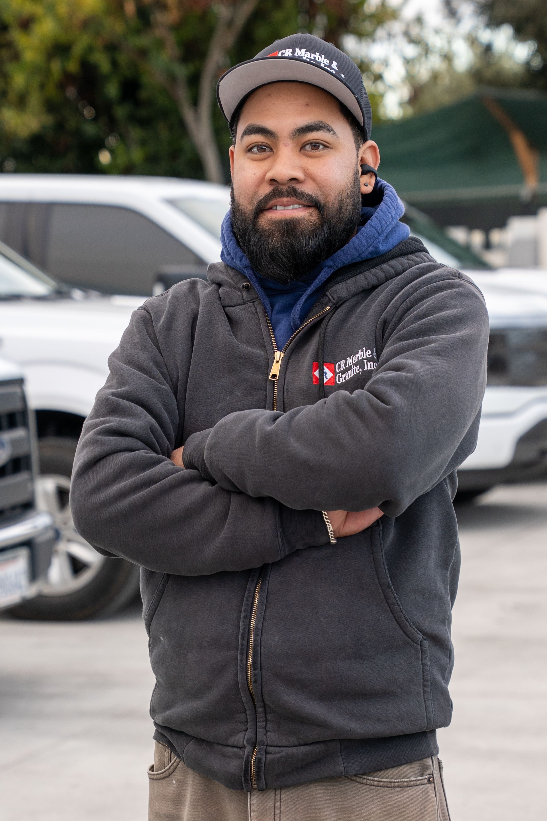 A man with a beard is standing in a parking lot with his arms crossed.