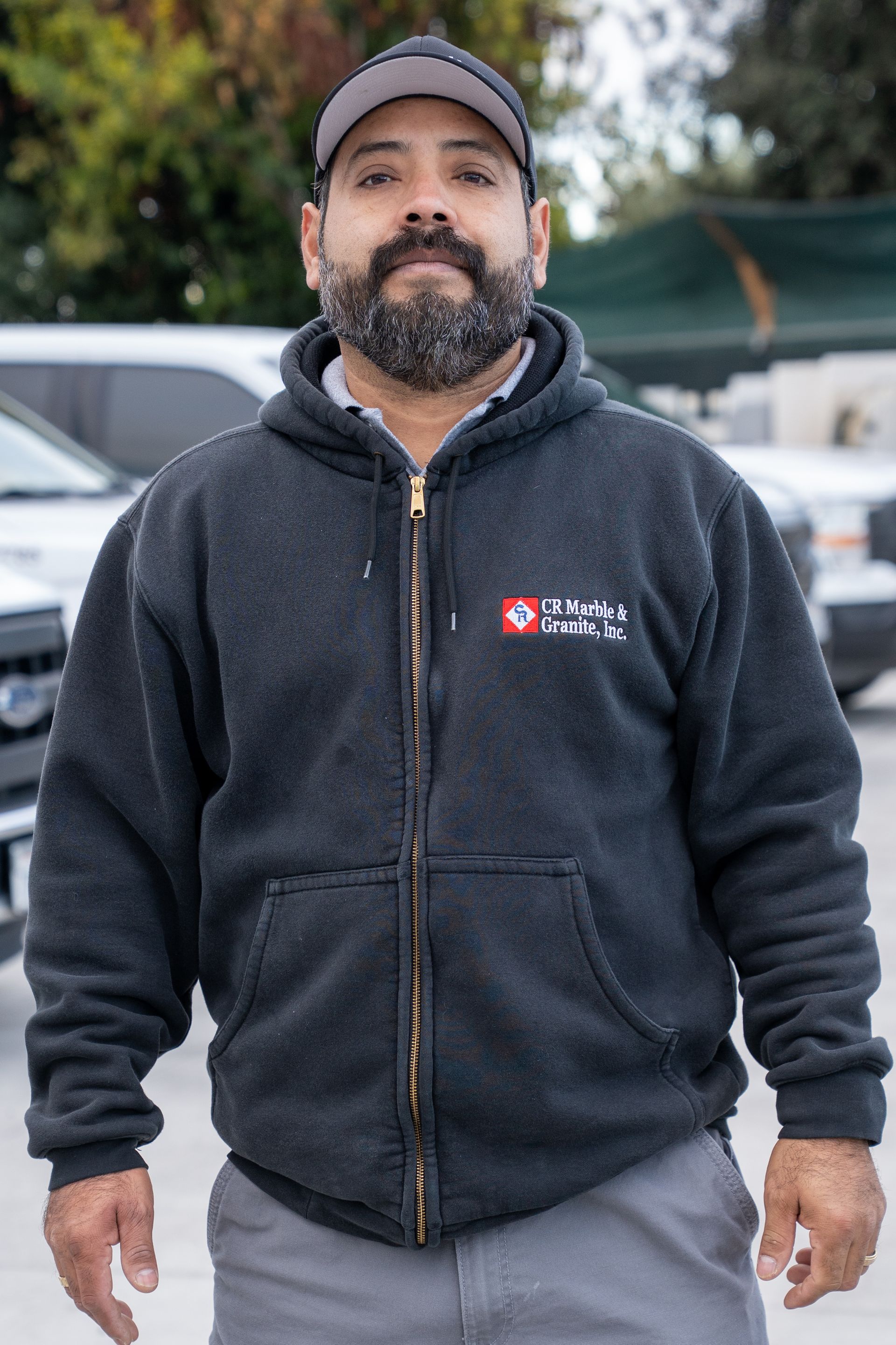 A man with a beard is wearing a black hoodie and a hat.
