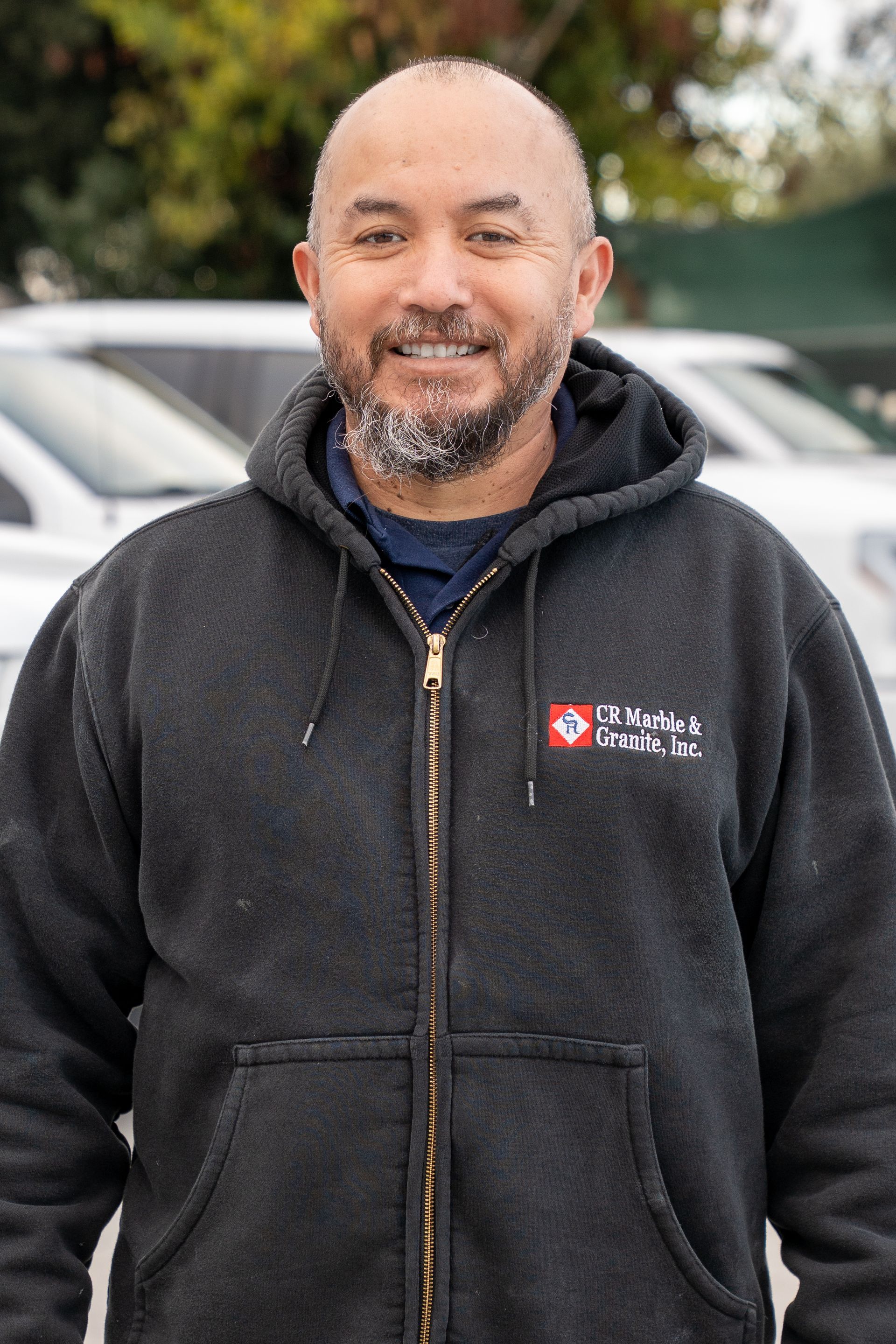 A man with a beard is wearing a black hoodie and smiling.